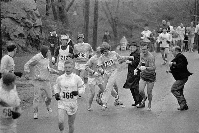 19 Apr 1967, Hopkinton, Massachusetts, USA --- In the Boston Marathon, one of two women running in the normally all-male race, K. Switzer, (261) of Syracuse, New York, gets past Marathon Director Bill Cloney, (in dark suit) here, who attempted to stop her from running. The dark-haired girl did not show up for physical examination required of all starters, (had she appeared at the starting line, she would never have been allowed to compete). She remained in the race, but was never seen near the finish line. --- Image by © Bettmann/CORBIS
